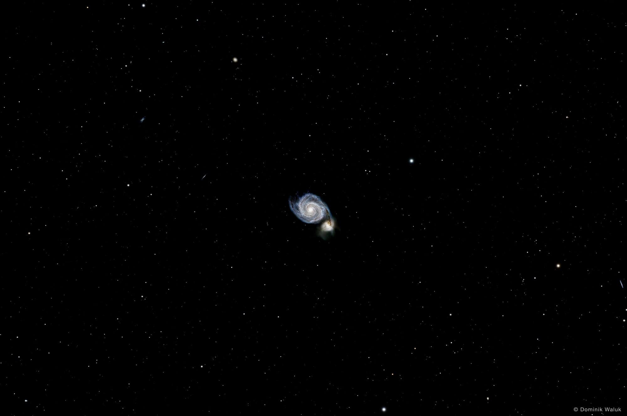 Die Whirlpool-Galaxie: eine Spiralgalaxie mit hellem Kern und einer kleineren Begleitgalaxie am Ende eines Spiralarms, in einem ruhigen Sternenfeld.