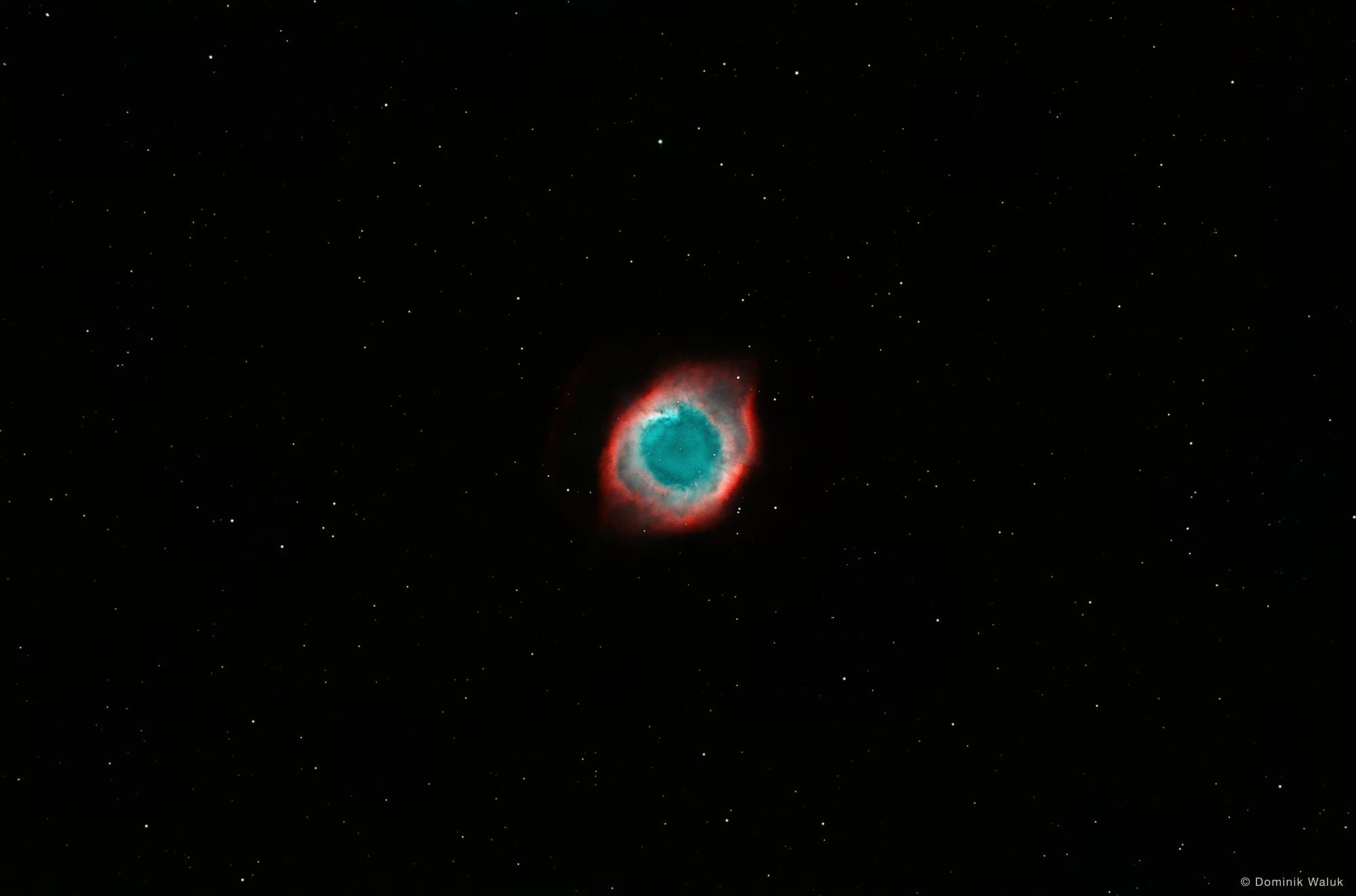 Der Helixnebel: ein rot und blaugrün leuchtender Ring vor einem dunklen Sternenfeld.