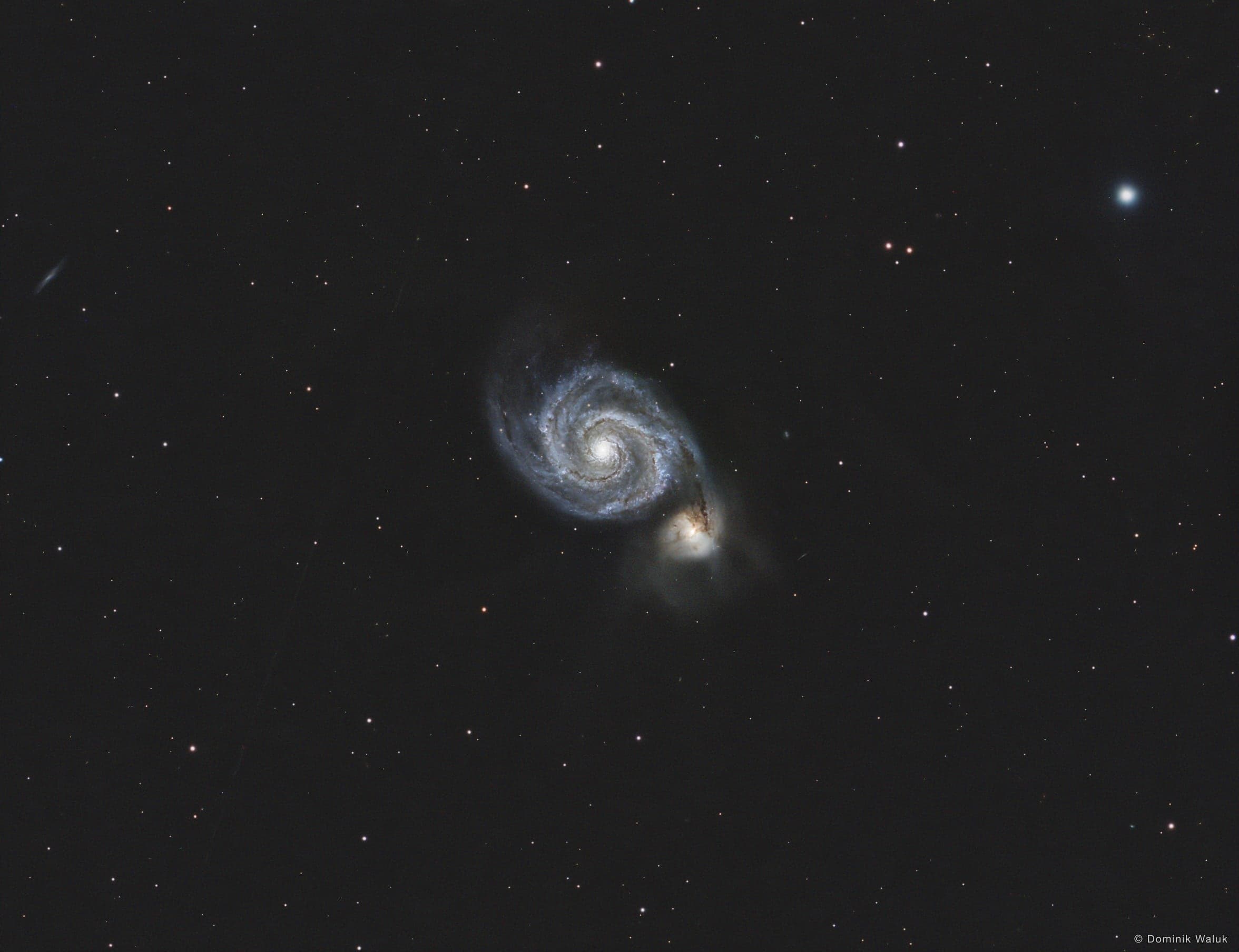 Die Whirlpool-Galaxie: eine Spiralgalaxie mit hellem Kern und einer kleineren Begleitgalaxie am Ende eines Spiralarms, in einem ruhigen Sternenfeld.