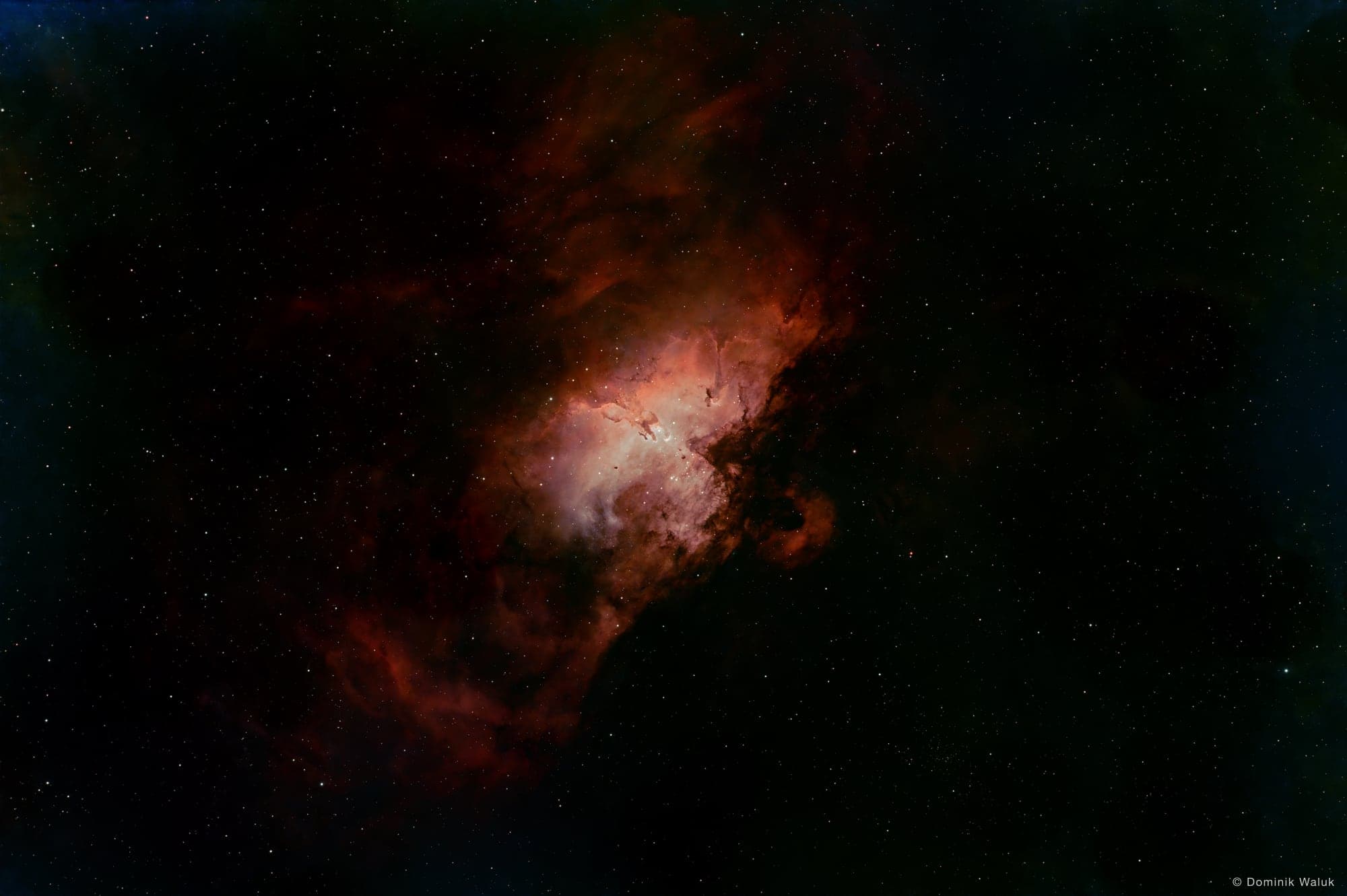 The Eagle Nebula: glowing orange and pink gas with dark pillars of dust at its centre, surrounded by reddish nebulosity.