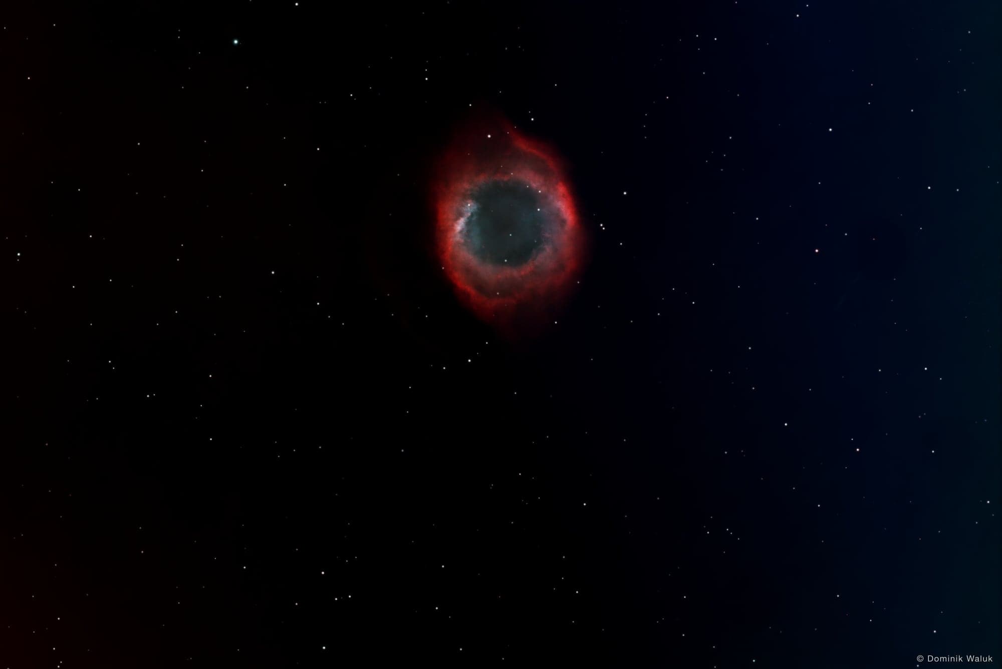 The Helix Nebula: a red and blue-green glowing ring against a dark field of stars.