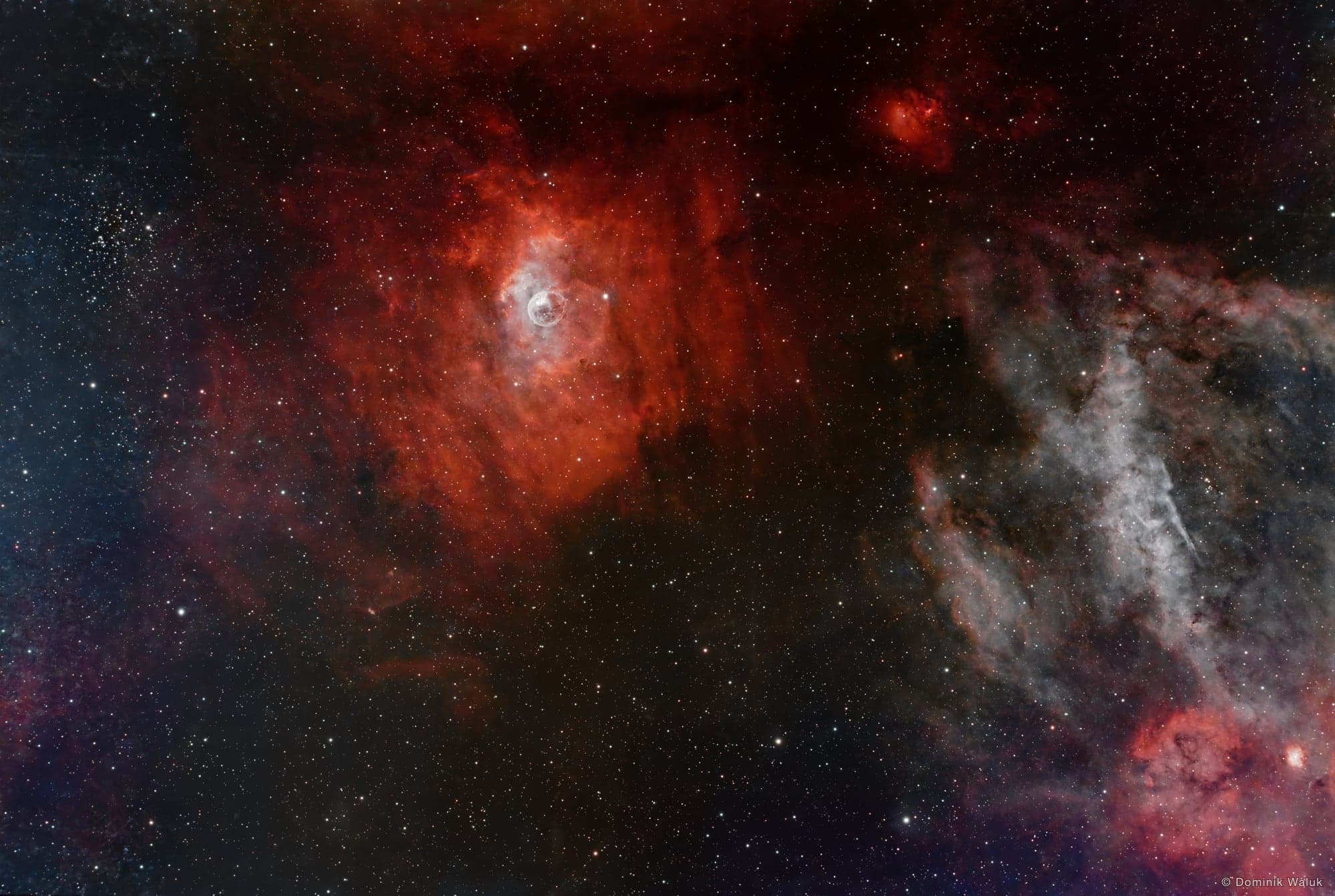 The Bubble Nebula: a delicate bubble of gas inside a large red-orange cloud, with grey veils of dust to the right.