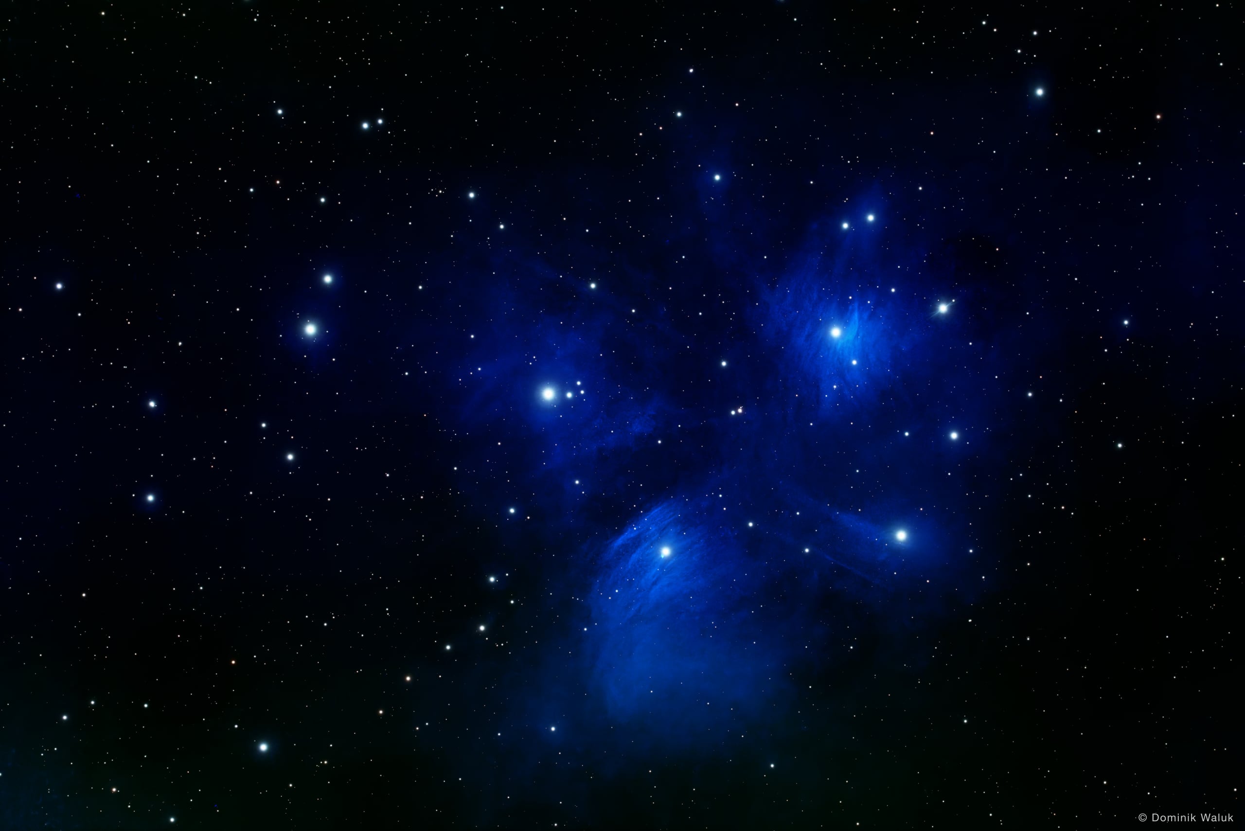 Die Plejaden: eine Gruppe heller blauer Sterne, eingehüllt in blau leuchtende Staubschleier.