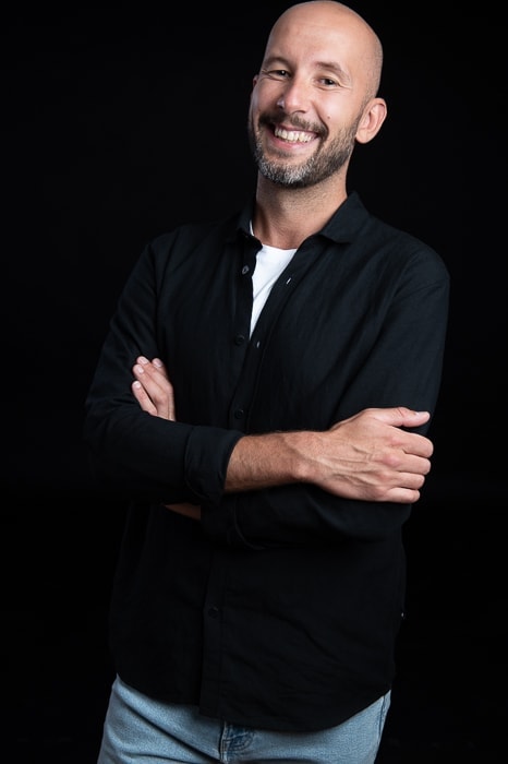 Dominik Waluk, lächelnd, mit verschränkten Armen vor schwarzem Hintergrund.