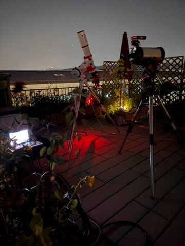 Zwei Teleskope auf Stativen auf der Dachterrasse bei Nacht, der Boden rot beleuchtet, daneben ein aufgeklappter Laptop.